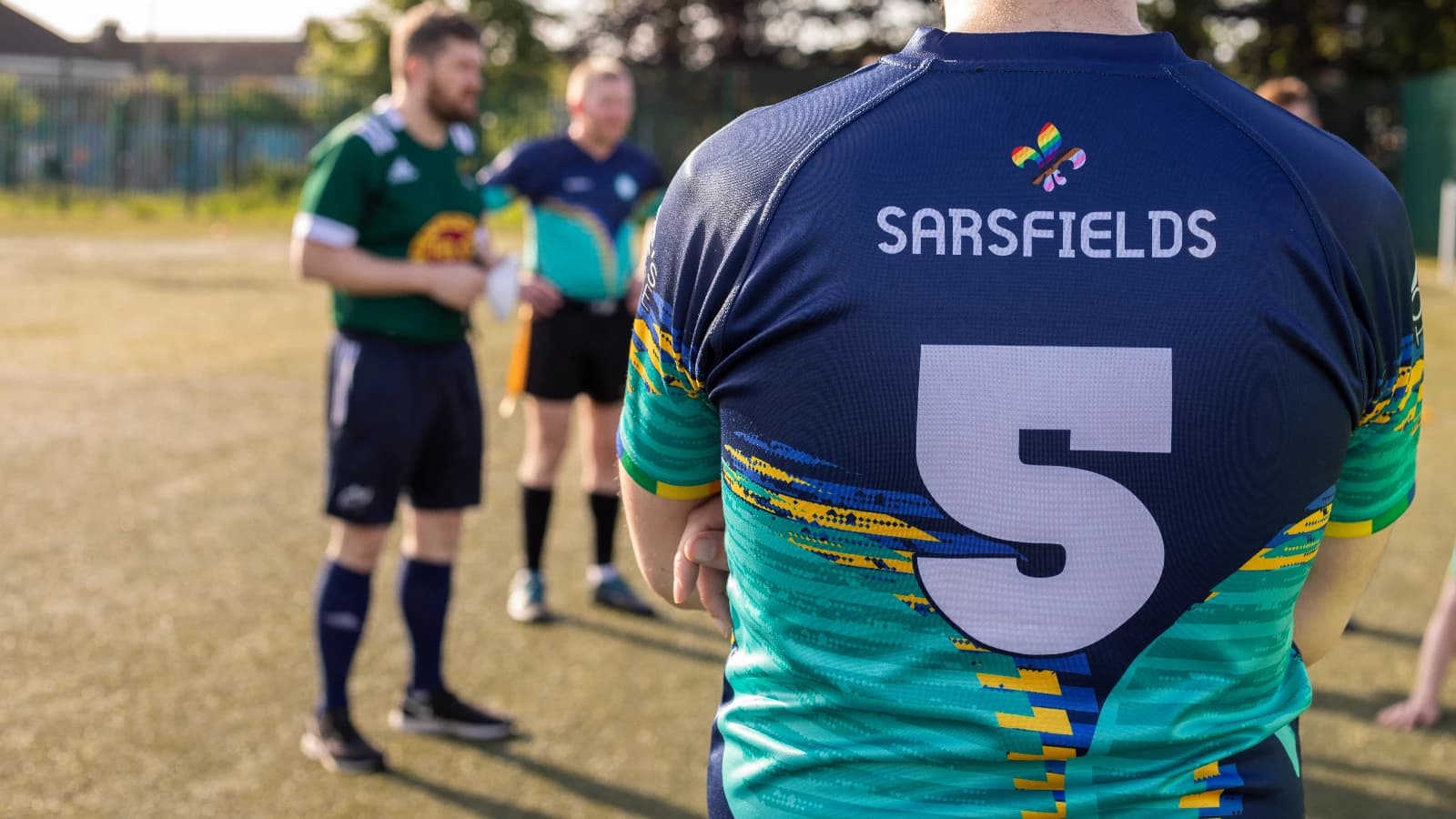 A Sarsfields Rugby player in the navy and teal club jersey with teammates on the pitch